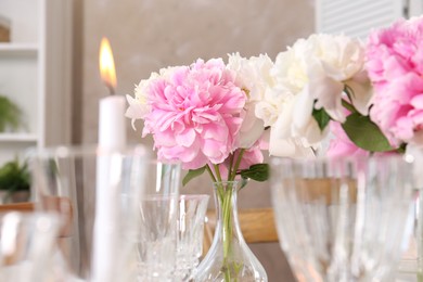 Photo of Stylish table setting with beautiful peonies and burning candle indoors, closeup