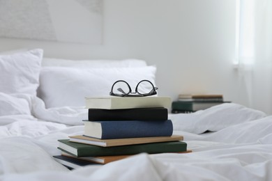Photo of Hardcover books and glasses on bed indoors