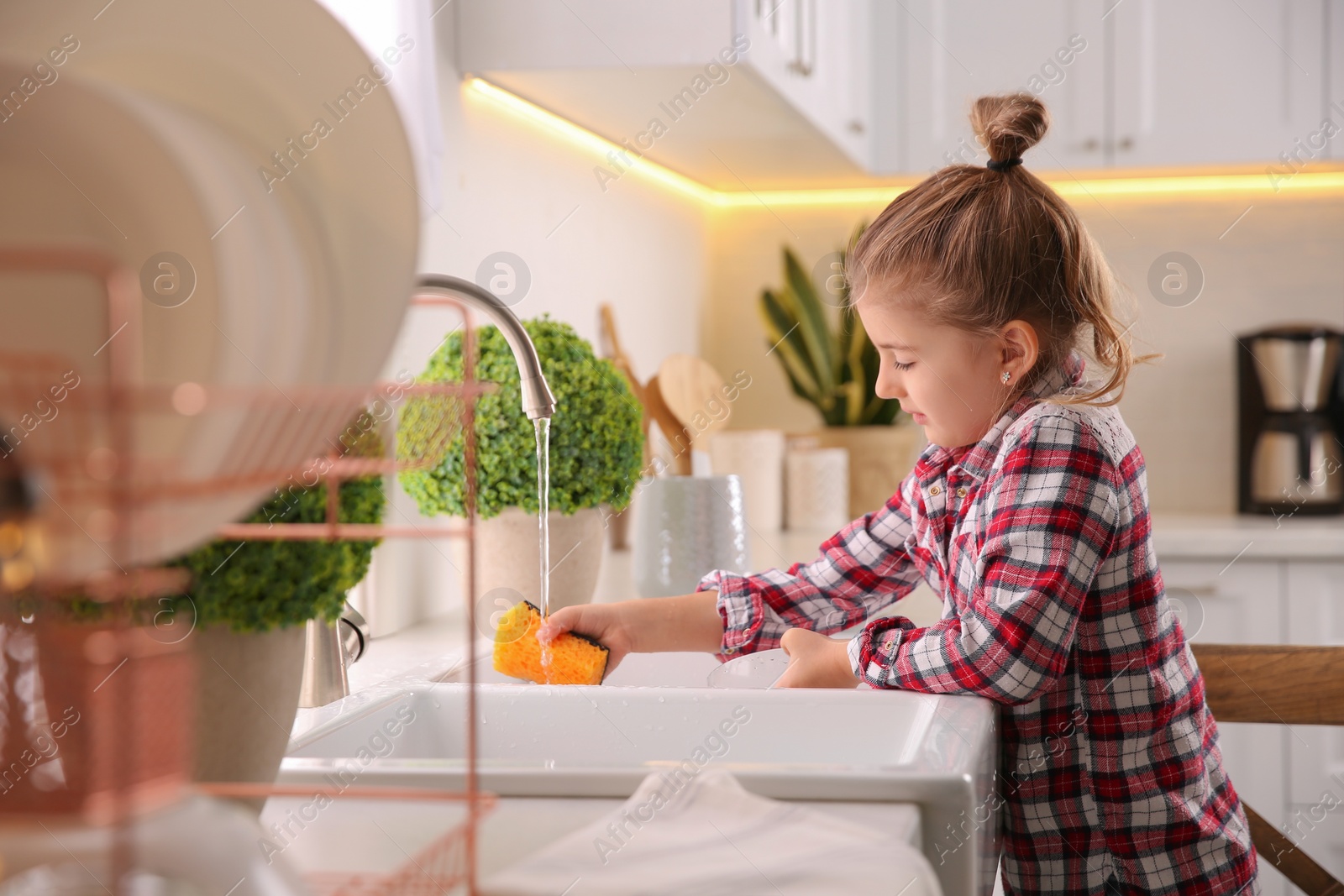 Photo of Little girl washing dishes in kitchen at home