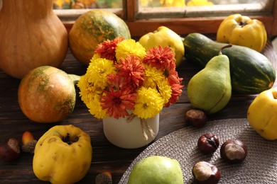 Photo of Beautiful colorful chrysanthemum flowers, pumpkins, quinces, pears and chestnuts on wooden table. Autumn still life