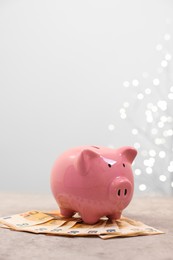 Piggy bank with euro banknotes on grey table against blurred lights, space for text