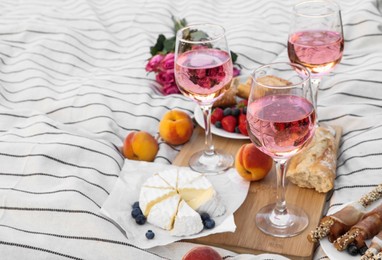 Glasses of delicious rose wine, flowers and food on white picnic blanket