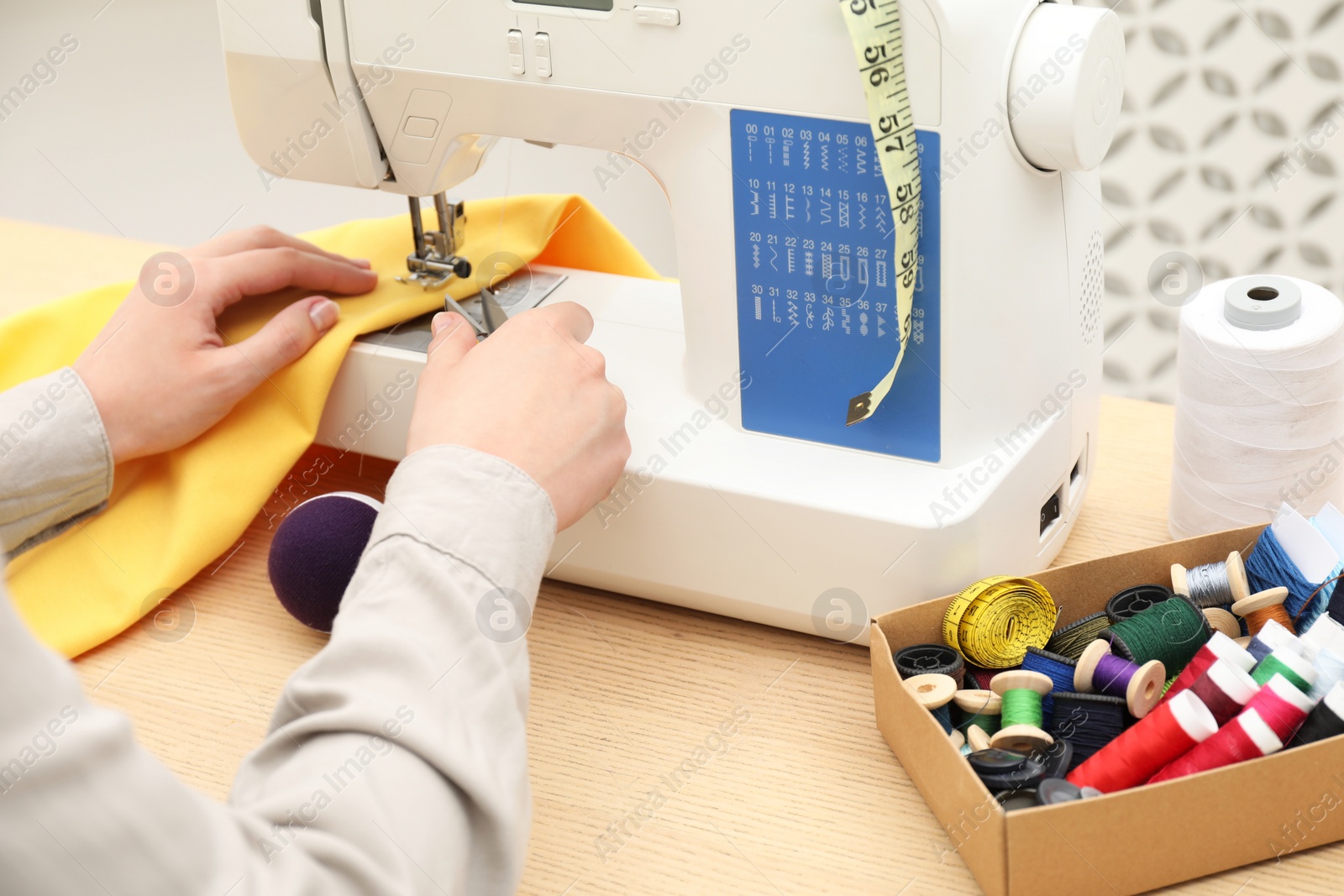 Photo of Seamstress working with sewing machine at wooden table indoors, closeup