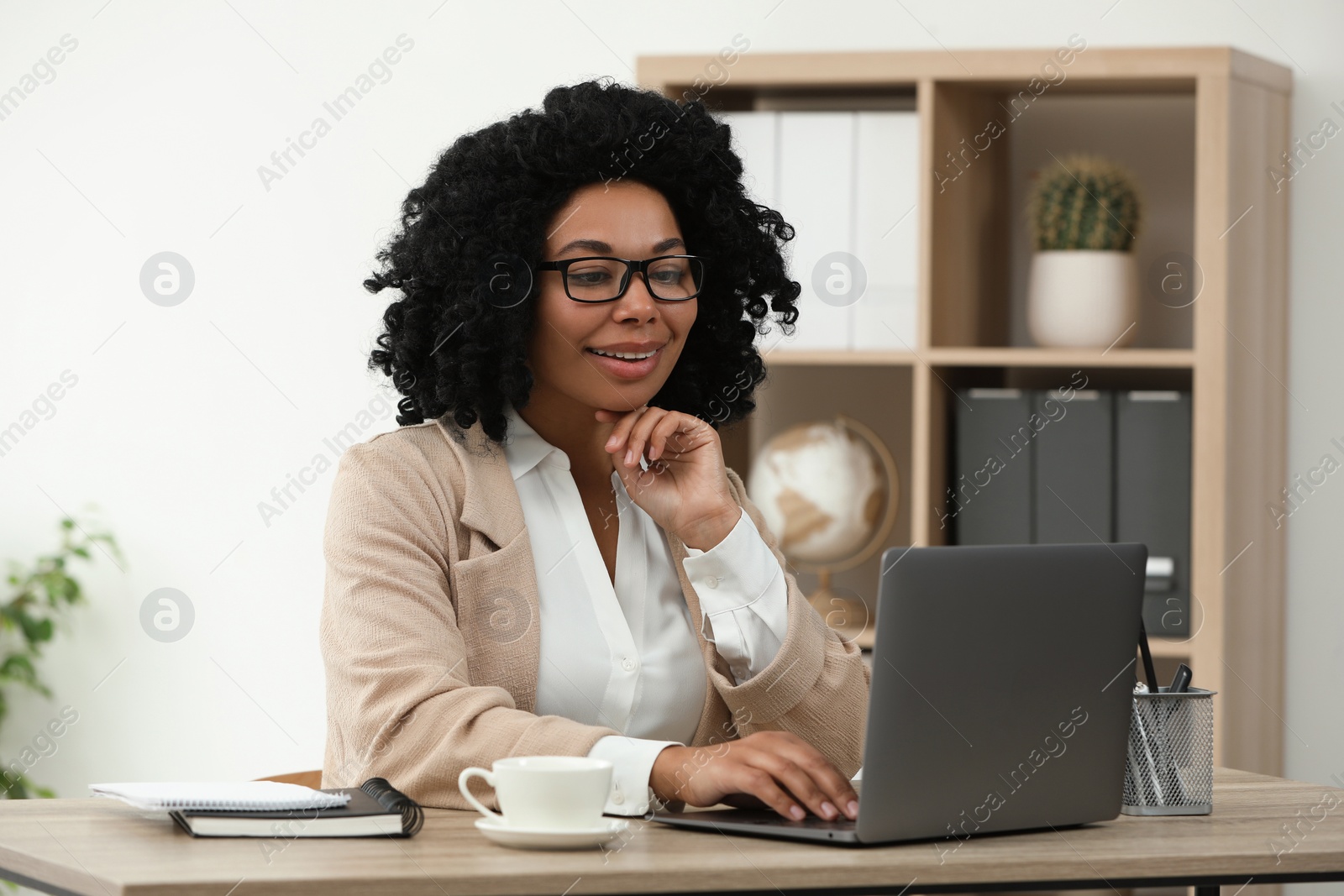 Photo of Happy young woman using laptop at wooden desk indoors