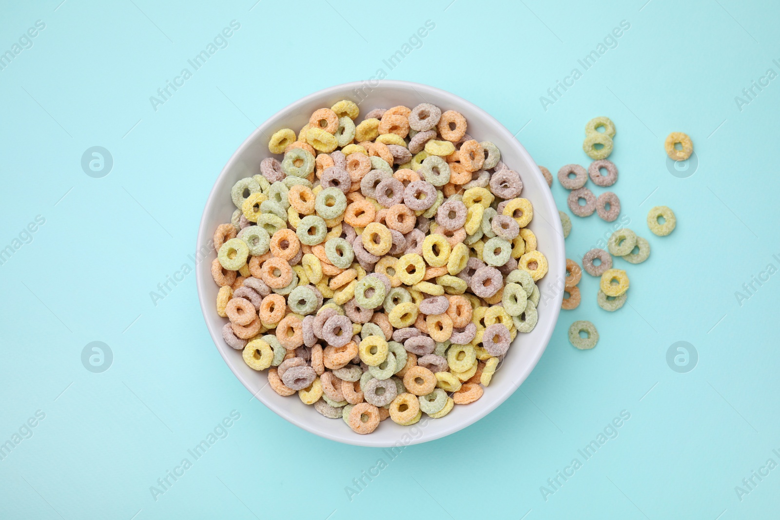 Photo of Tasty cereal rings in bowl on light blue table, top view