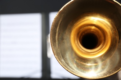 Trumpet and blurred music note sheets on background, closeup. Space for text