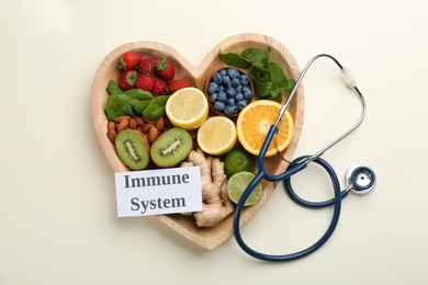 Heart shaped tray of healthy products, stethoscope and card with text Immune System on beige background, flat lay