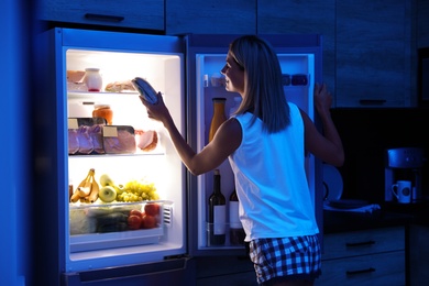 Photo of Woman taking sandwich out of refrigerator in kitchen at night