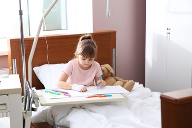 Photo of Little child with intravenous drip drawing in hospital bed