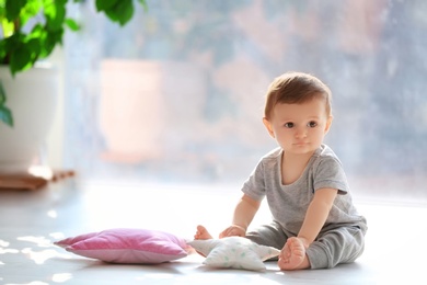 Cute baby sitting on floor near window indoors