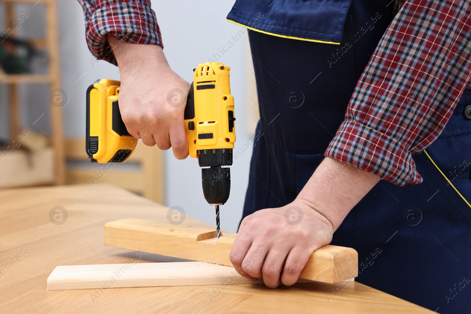 Photo of Young worker using electric drill at table in workshop, closeup
