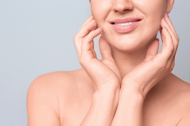 Beautiful woman with clean skin touching her face on light background