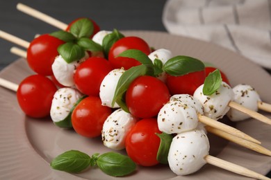 Photo of Caprese skewers with tomatoes, mozzarella balls, basil and spices on plate, closeup