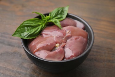 Photo of Bowl of raw chicken liver with basil on wooden table, closeup