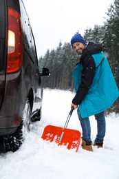 Man cleaning snow with shovel near stuck car outdoors