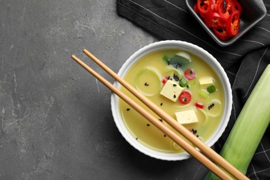 Photo of Bowl of delicious miso soup with tofu and chopsticks served on grey table, flat lay. Space for text