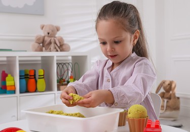 Cute little girl playing with bright kinetic sand at table in room