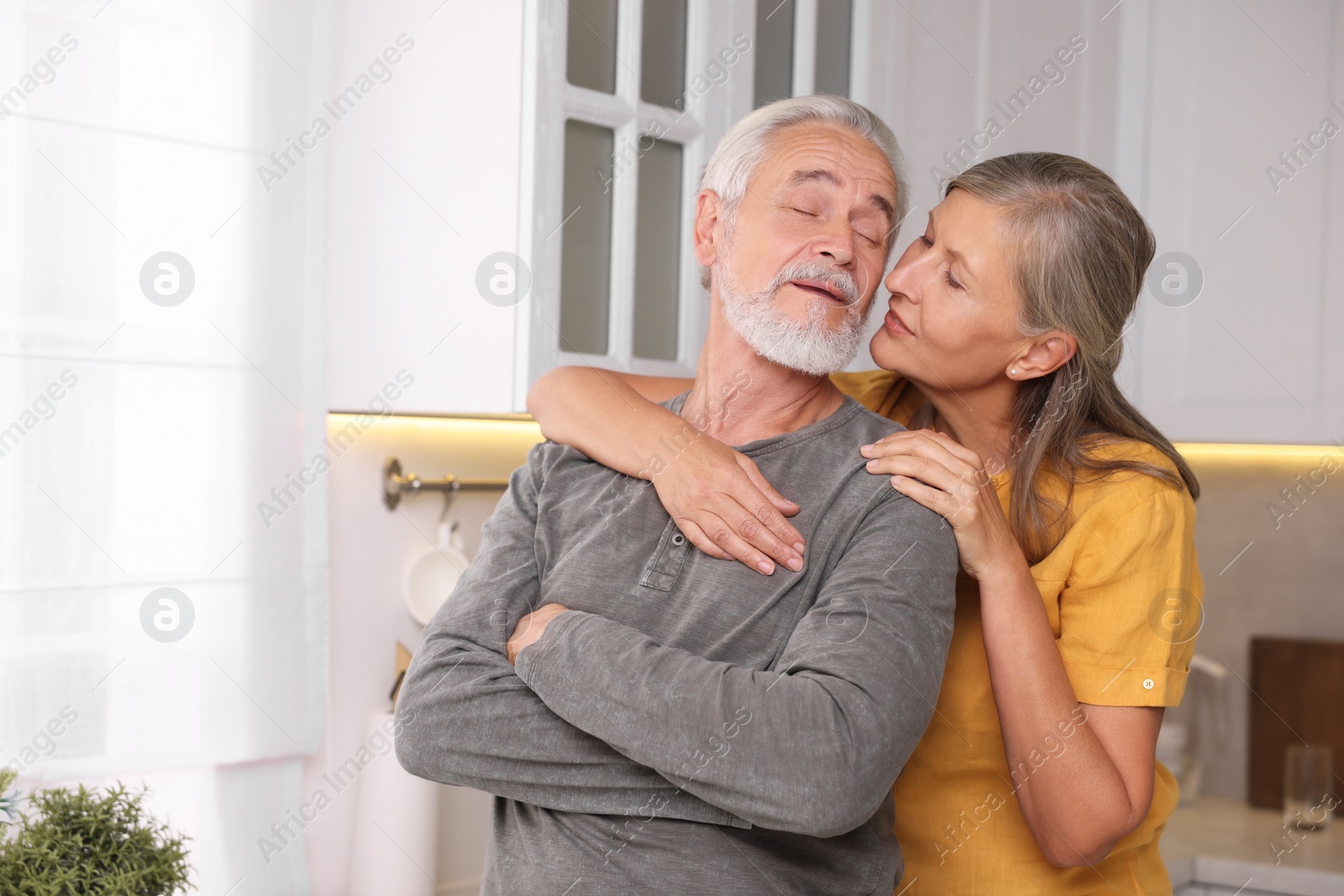Photo of Senior woman kissing her beloved man in kitchen, space for text