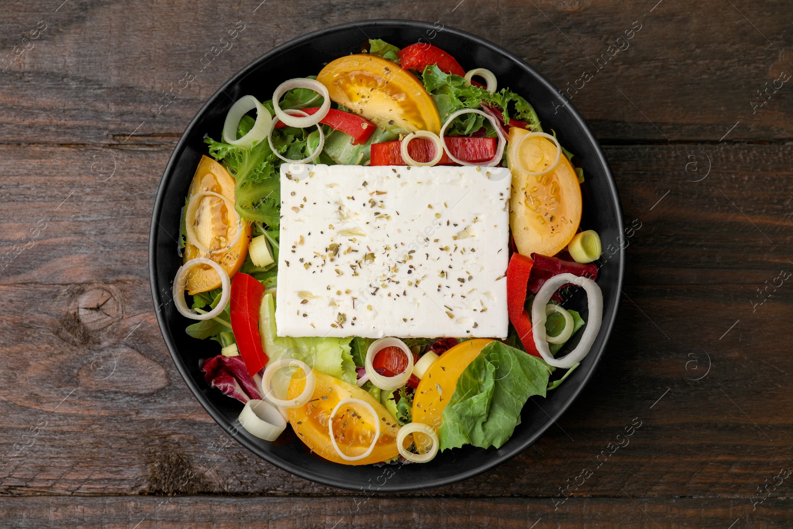 Photo of Bowl of tasty salad with leek and cheese on wooden table, top view