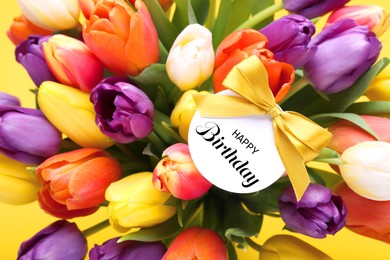 Image of Beautiful bouquet of tulip flowers with Happy Birthday card on yellow background, closeup