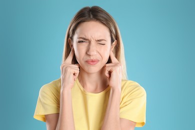 Emotional young woman covering her ears with fingers on light blue background