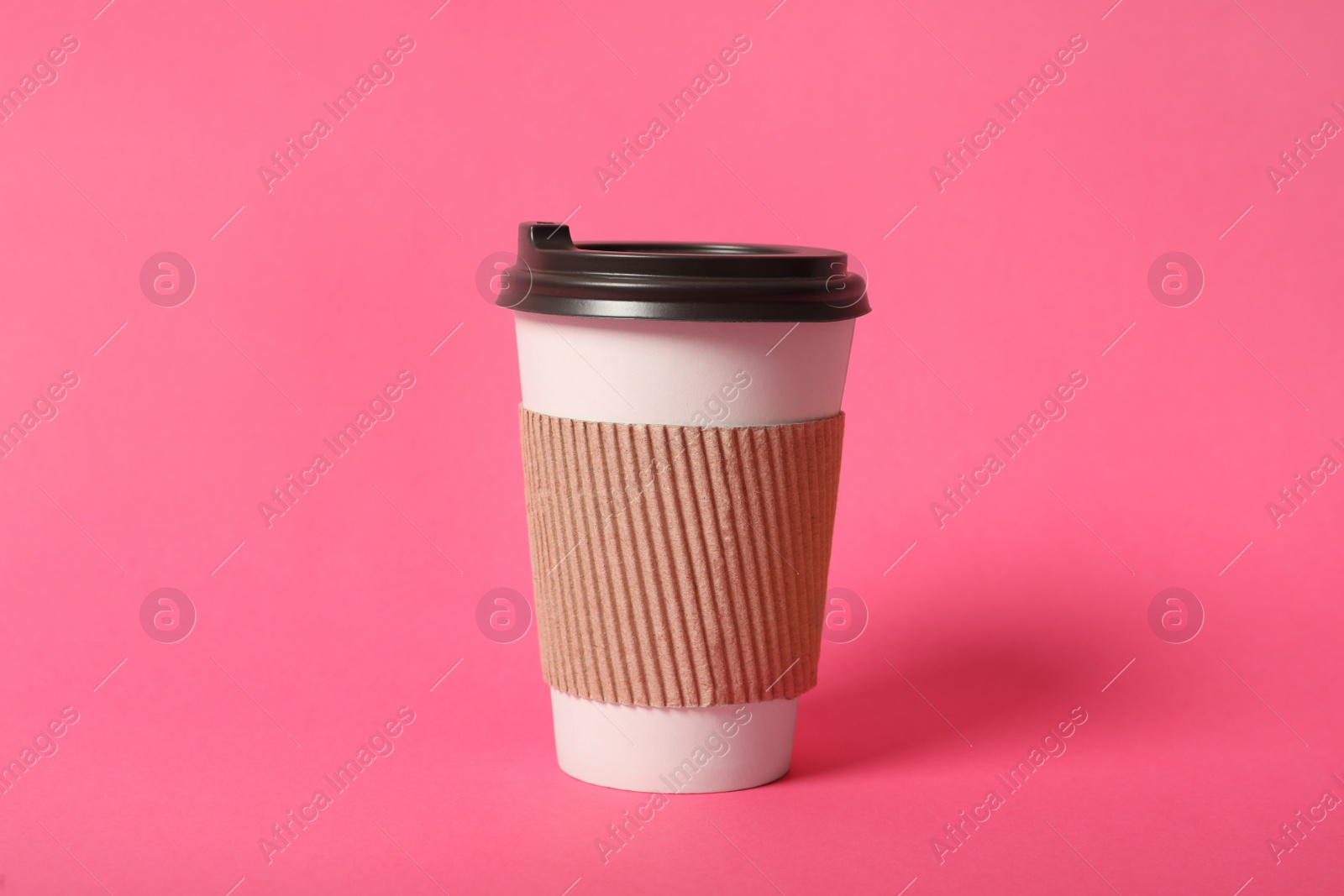 Photo of Takeaway paper coffee cup with cardboard sleeve on pink background
