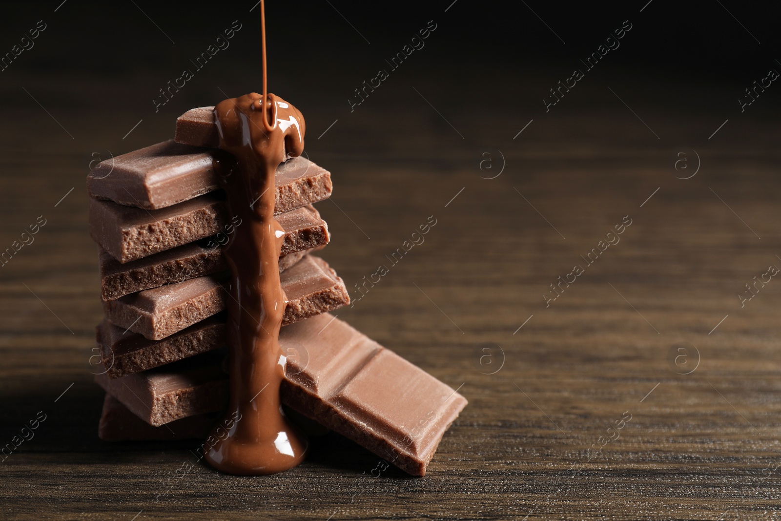 Photo of Pouring tasty milk chocolate paste onto pieces on wooden table, closeup. Space for text