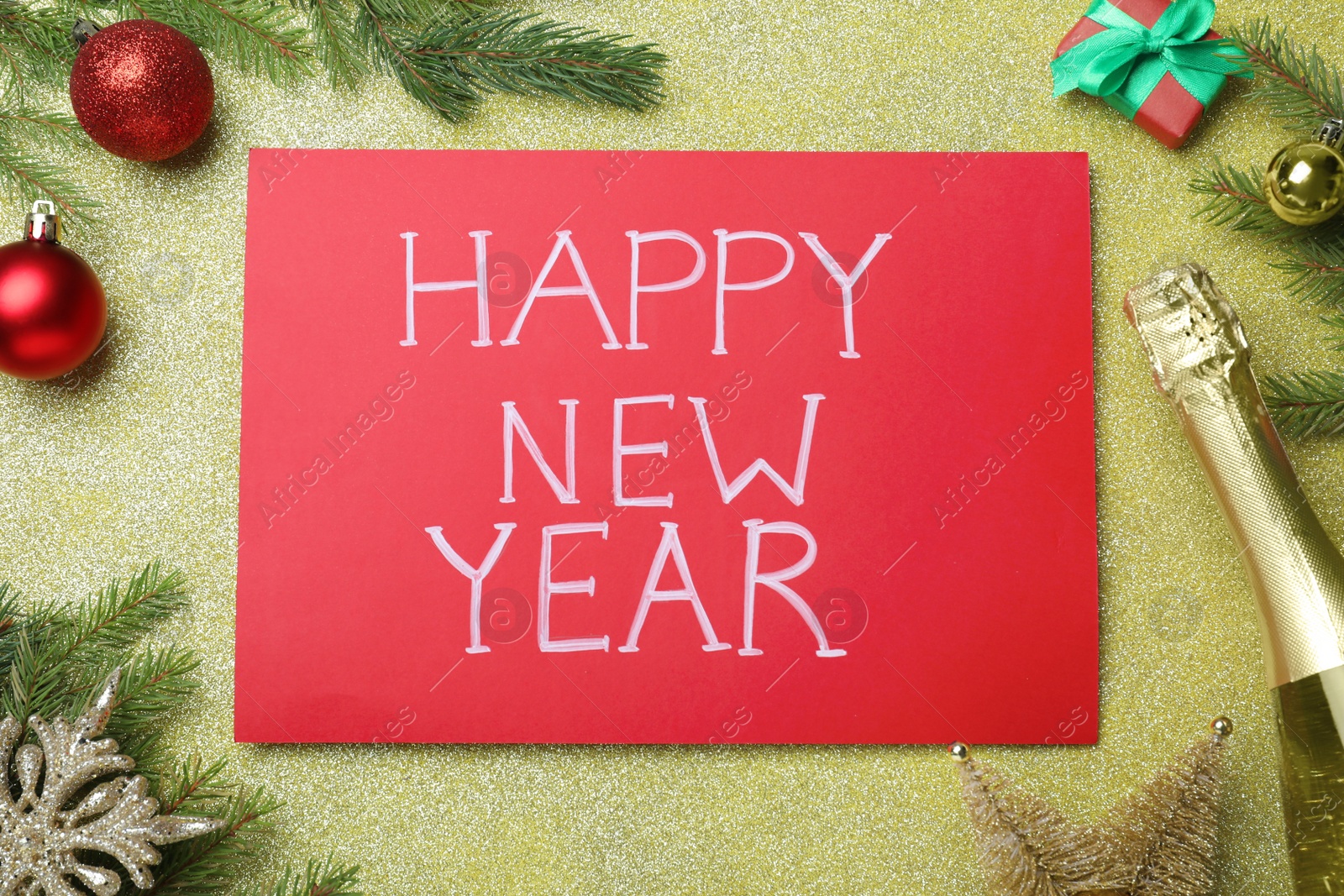 Photo of Happy New Year greeting card. Red paper with phrase and decor on shiny background, flat lay