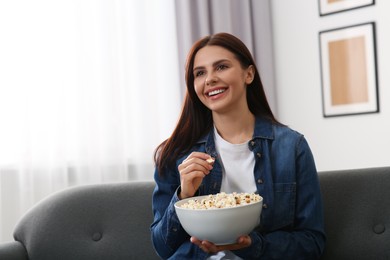 Photo of Happy woman with bowl of popcorn watching TV at home