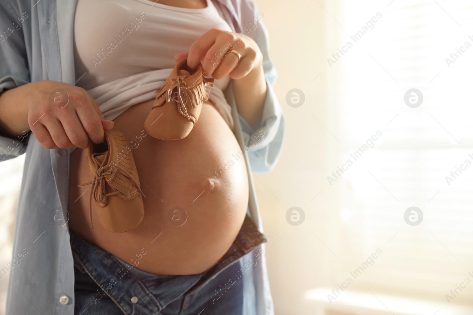 Photo of Young pregnant woman with baby's shoes indoors, closeup. Space for text