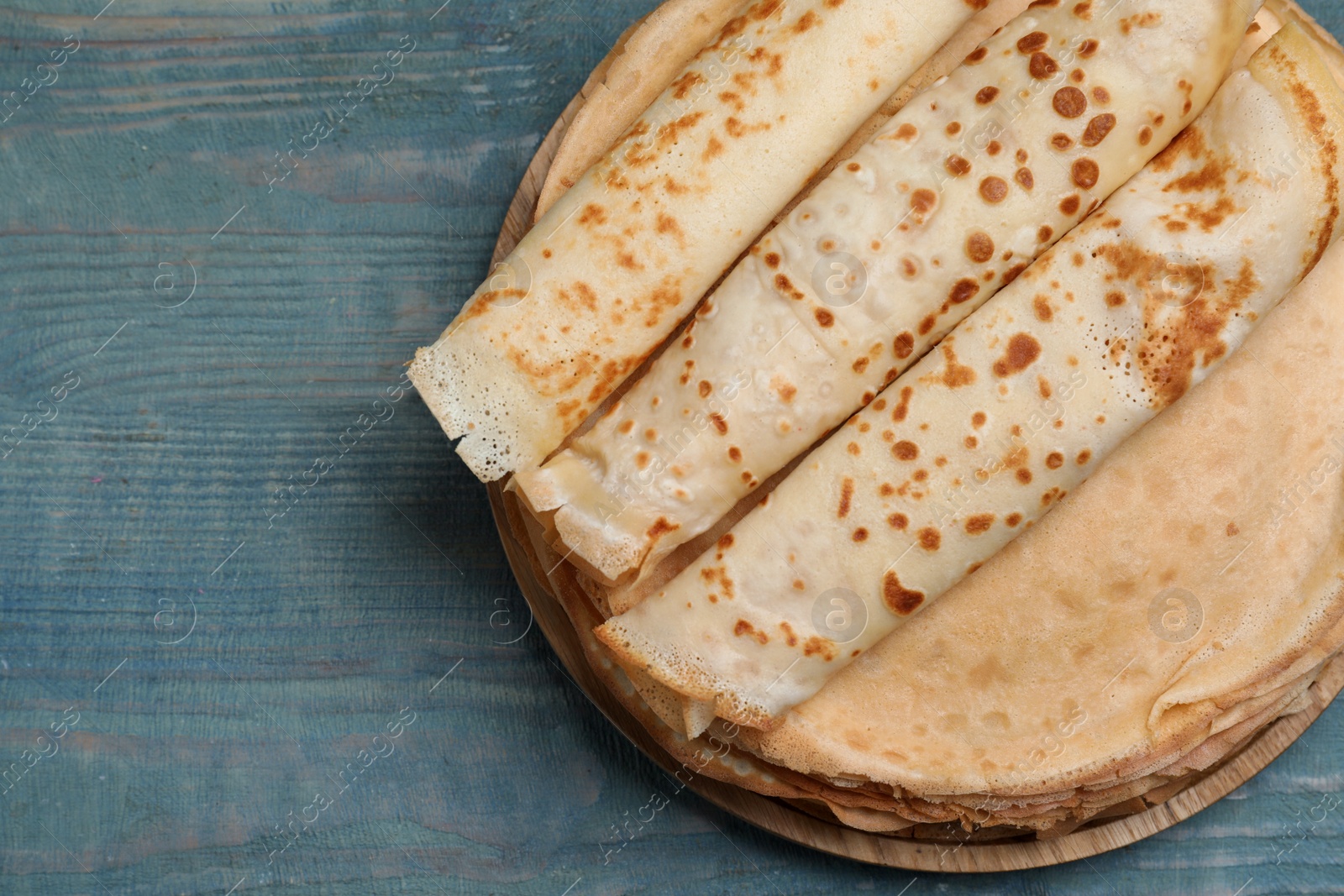 Photo of Delicious crepes on blue wooden table, top view. Space for text