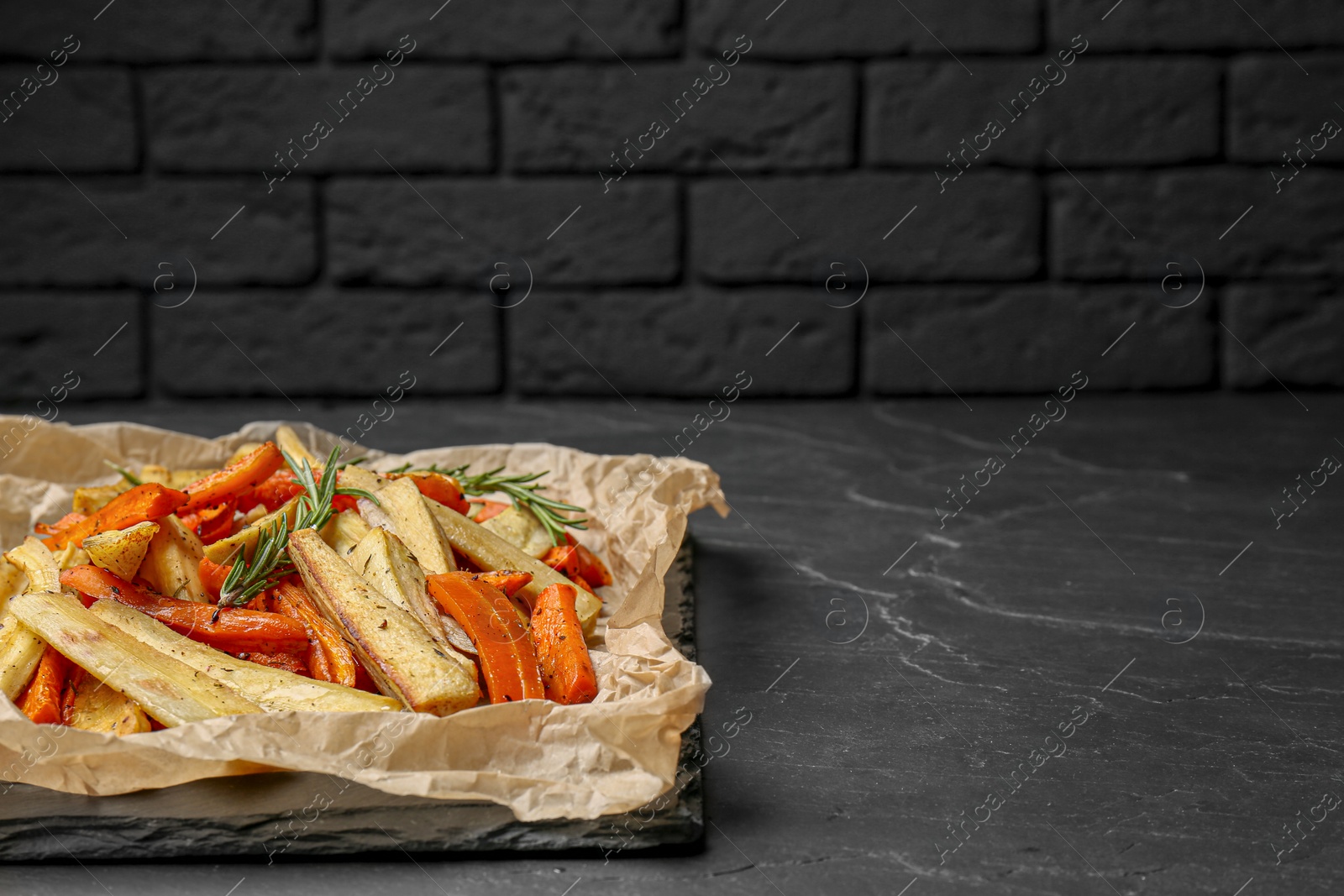 Photo of Parchment with tasty baked parsnip and bell pepper on dark grey table, space for text