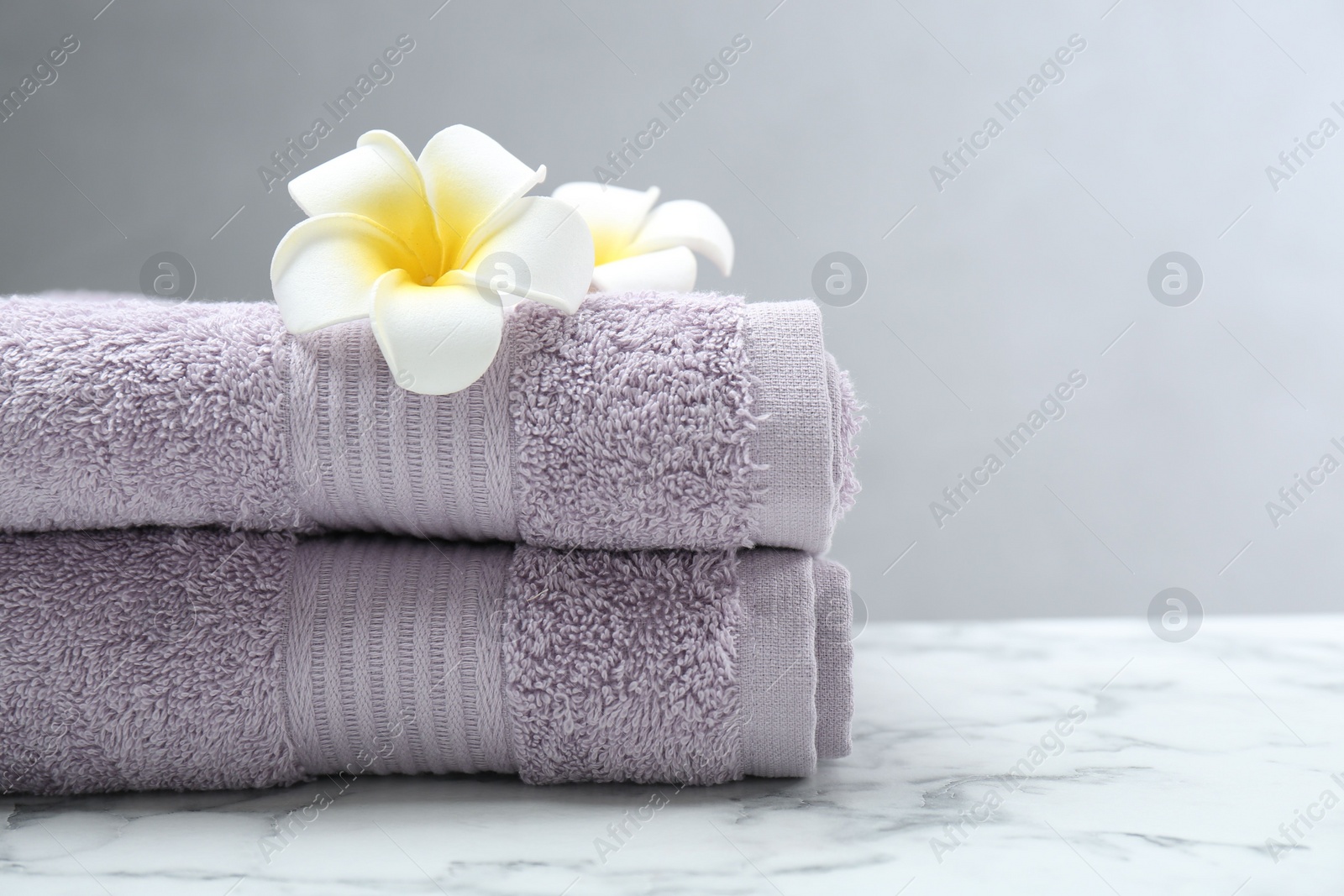 Photo of Violet terry towels and plumeria flowers on white marble table, closeup. Space for text