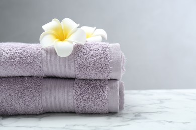 Violet terry towels and plumeria flowers on white marble table, closeup. Space for text