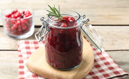 Photo of Fresh cranberry sauce in glass jar and rosemary on light wooden table