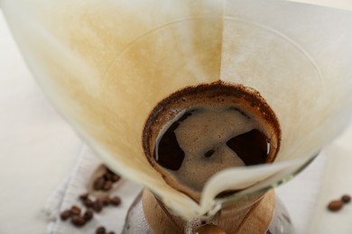 Photo of Brewing aromatic drip coffee in chemex coffeemaker with paper filter on table, closeup