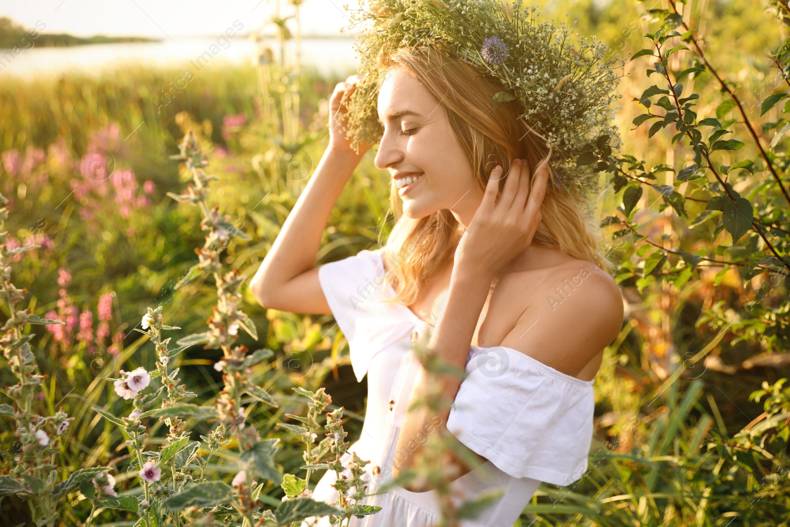 Photo of Young woman wearing wreath made of beautiful flowers outdoors on sunny day