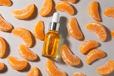 Aromatic tangerine essential oil in bottle and citrus fruit on grey table, flat lay
