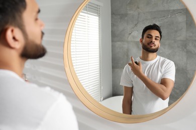 Photo of Man spraying luxury perfume near mirror indoors