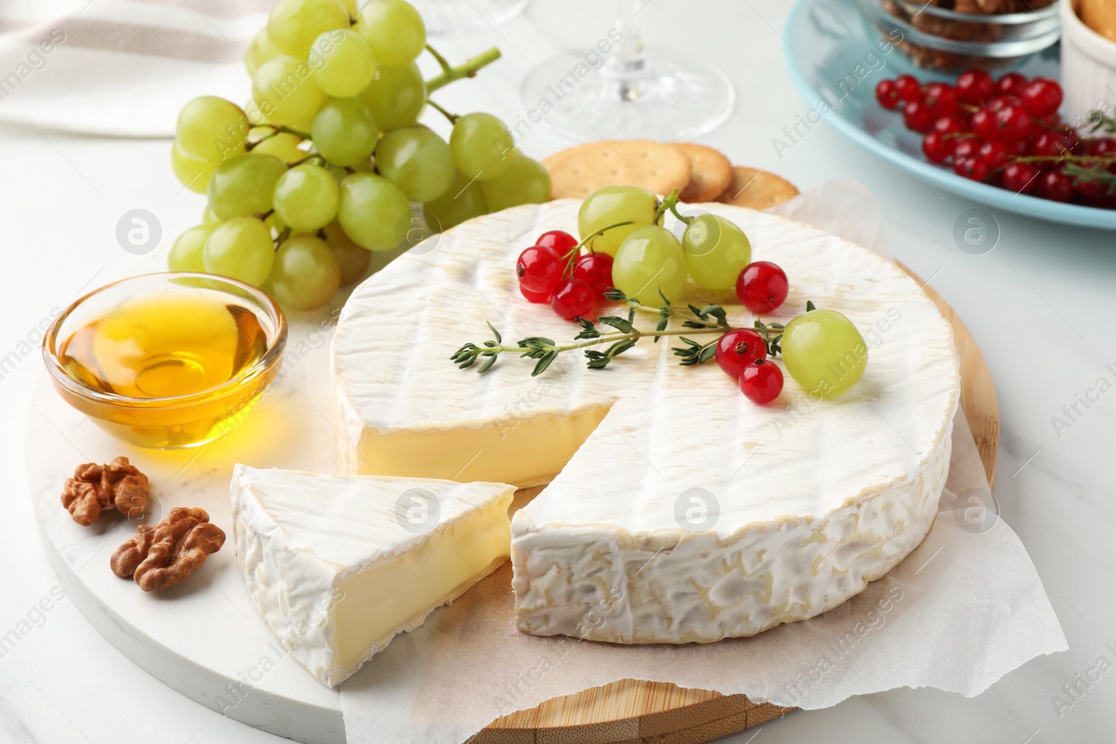 Photo of Brie cheese served with honey and berries on white table