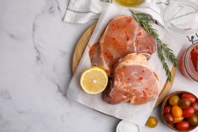 Flat lay composition with raw marinated meat, lemon and rosemary on white marble table. Space for text