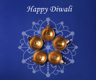 Inscription Happy Diwali and clay lamps on color background, flat lay 