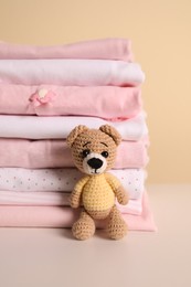 Photo of Stack of baby girl's clothes and toy bear on white table
