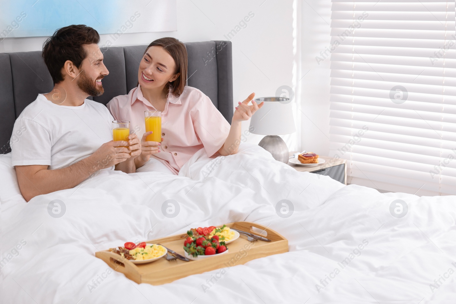 Photo of Happy couple eating tasty breakfast and talking in bed at home. Space for text