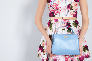 Young woman wearing floral print dress with stylish handbag on light background, closeup. Space for text