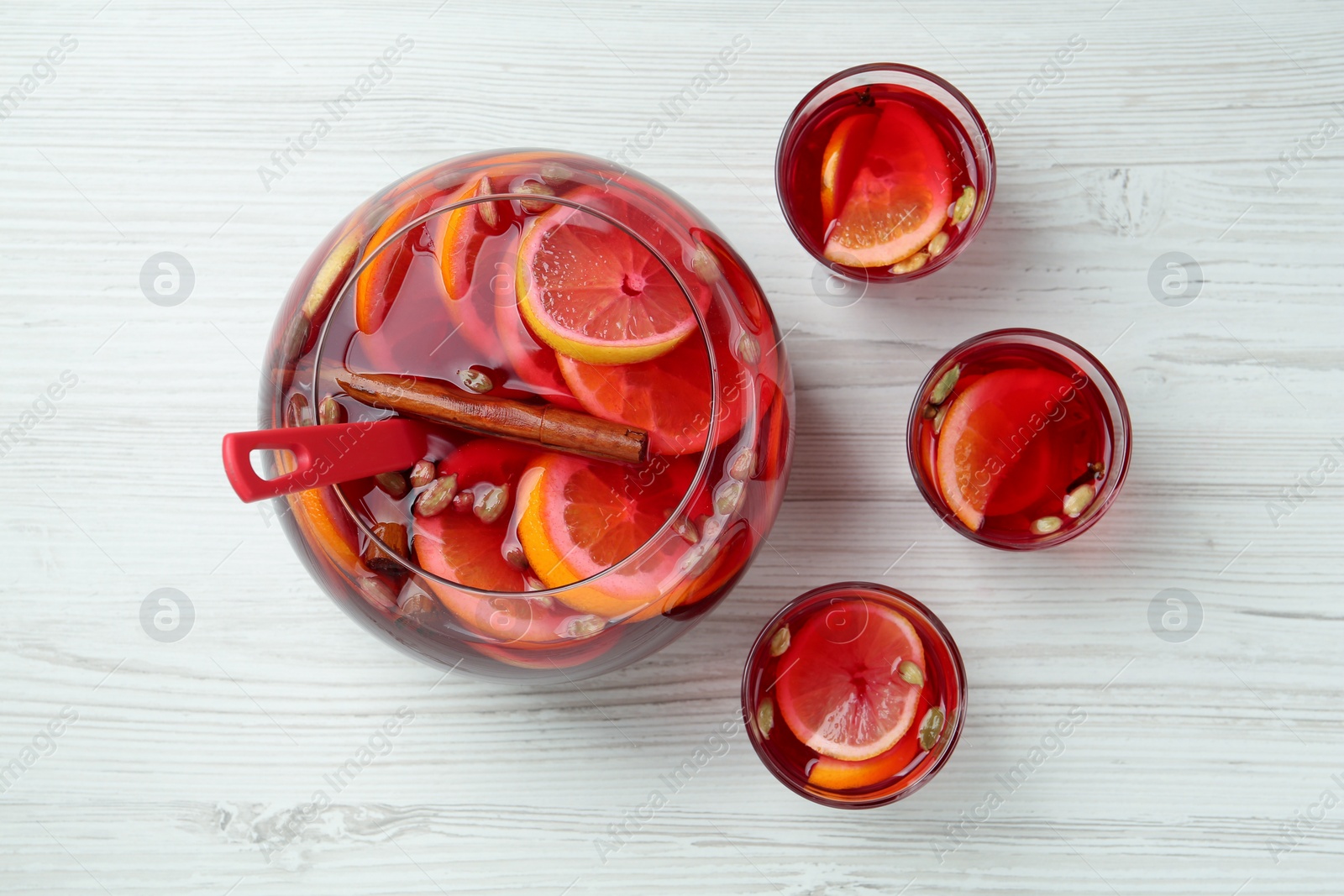 Photo of Glasses and bowl with aromatic punch drink on white wooden table, flat lay