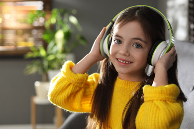 Photo of Cute little girl with headphones listening to audiobook at home