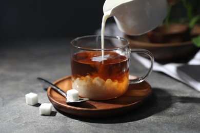 Photo of Pouring milk into cup of tea on grey table, closeup