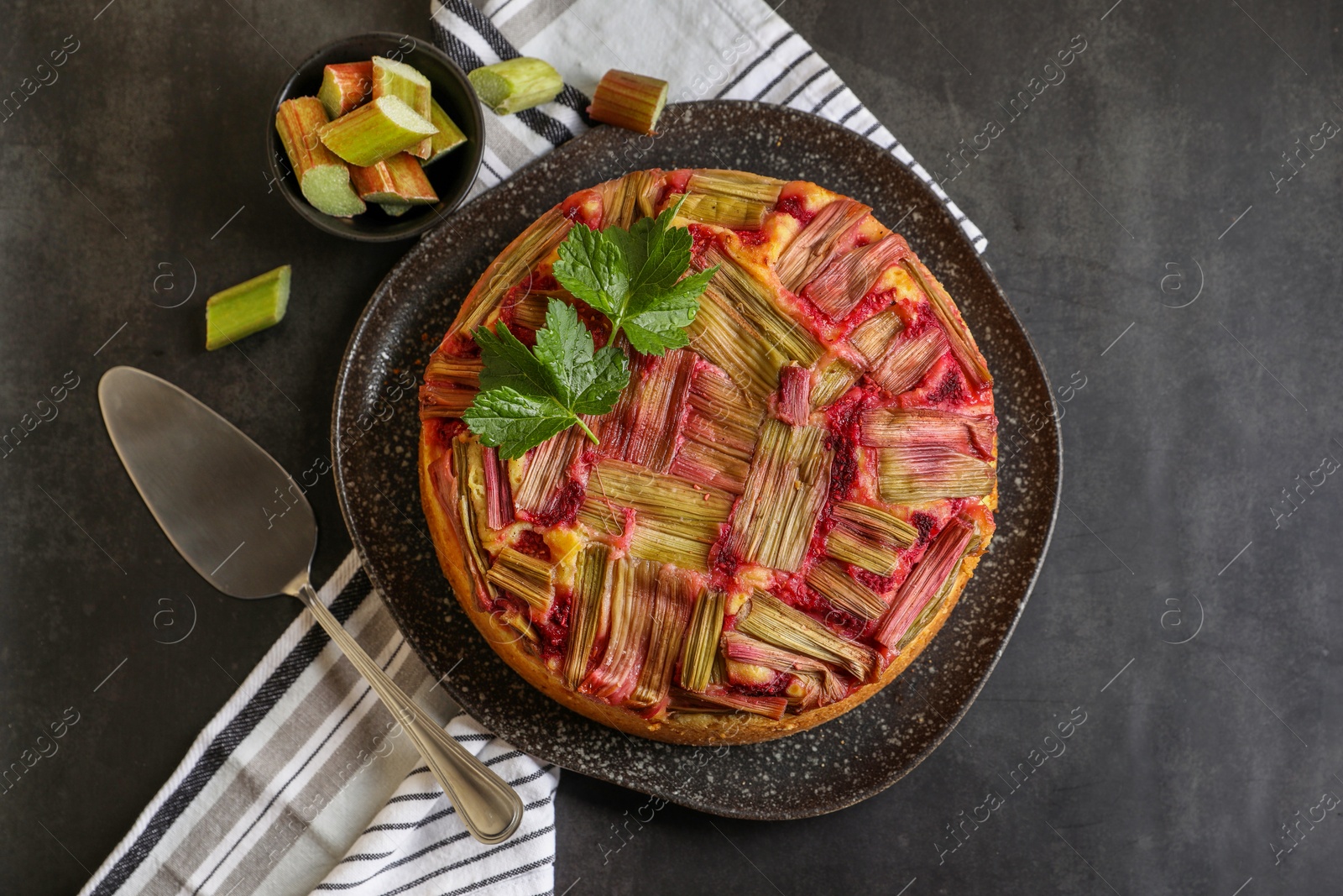 Photo of Freshly baked rhubarb pie, cut stalks and cake server on black table, flat lay