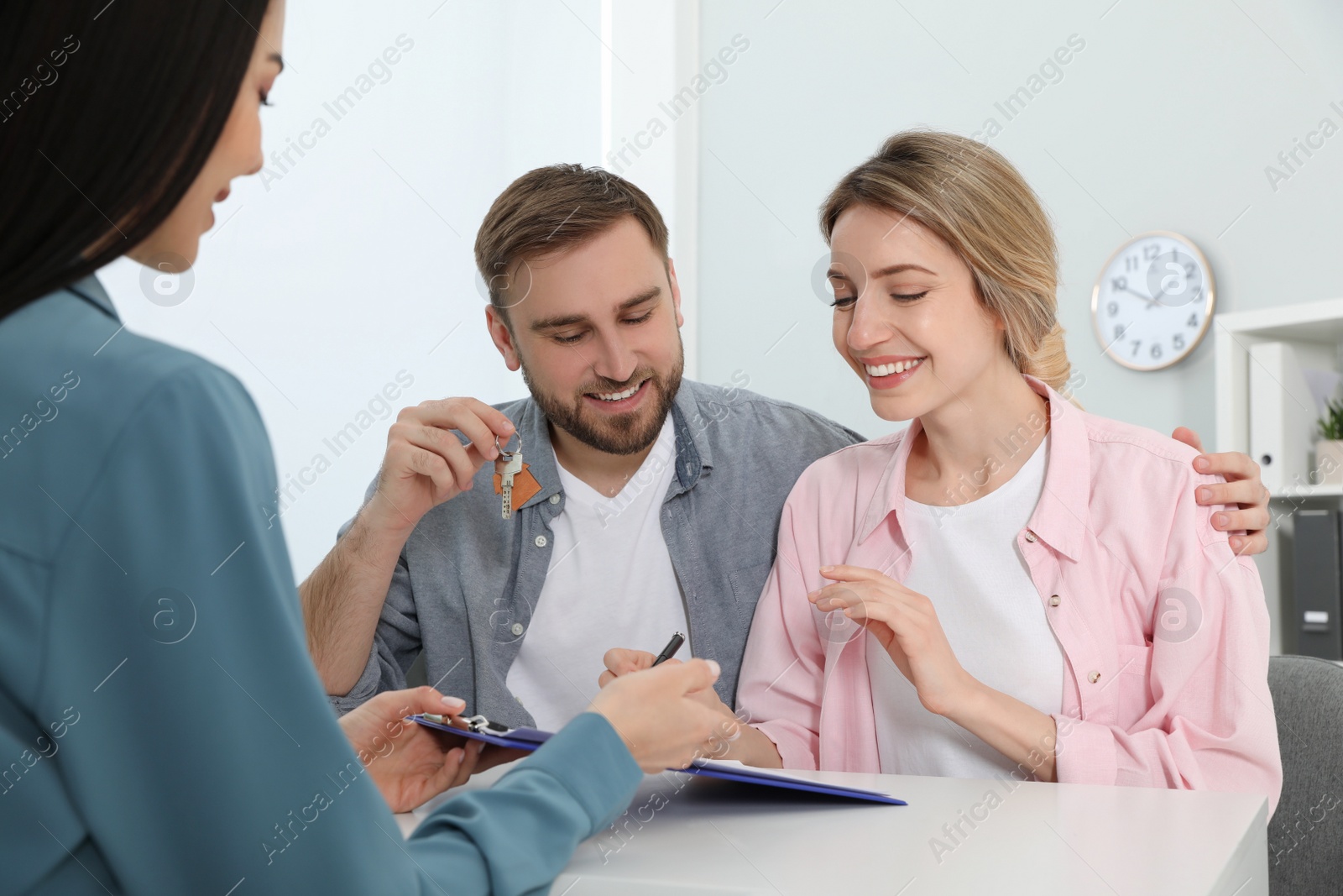 Photo of Happy young couple signing purchase contract in real estate agent's office. Man with new house key